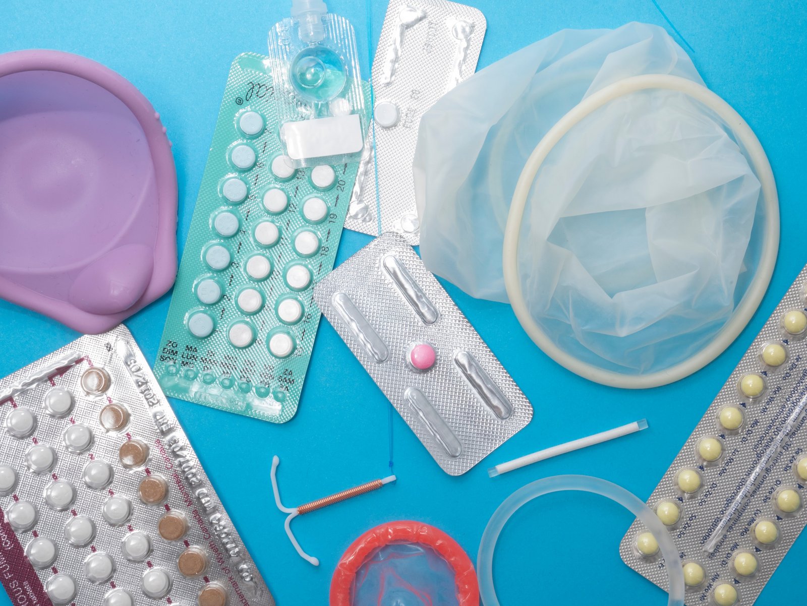A blue background on which lie various hormonal and hormone-free contraceptives for women
